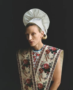 Model Maggie Maurer wearing a white bonnet and floral tunic against a black background for ODDA Magazine