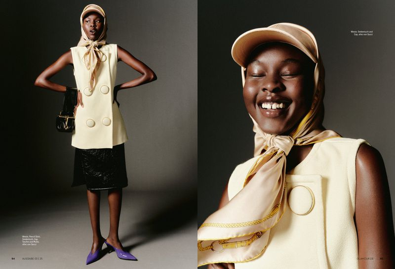 Fashion editorial shot of a Black female model in a cream-colored vest, headscarf, cap, and purple heels against a gray backdrop.