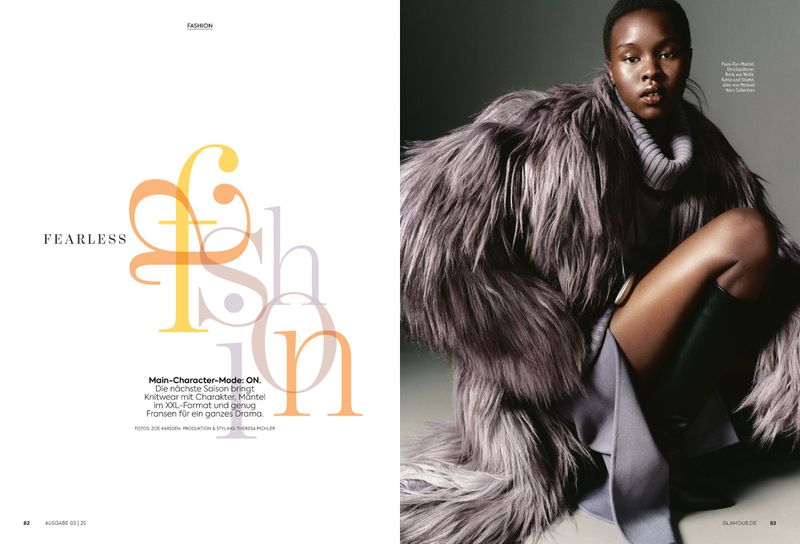 A dark-skinned woman wears a grey fur coat and black boots, sitting in a studio environment with the word 'Fashion' in the background.
