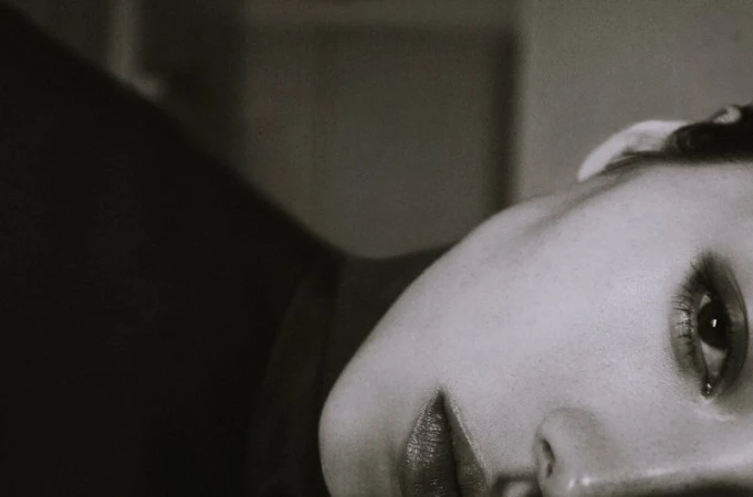 Close-up shot of a Black and White portrait of a woman laying down looking up with dramatic eye makeup and full lips in a photo studio.