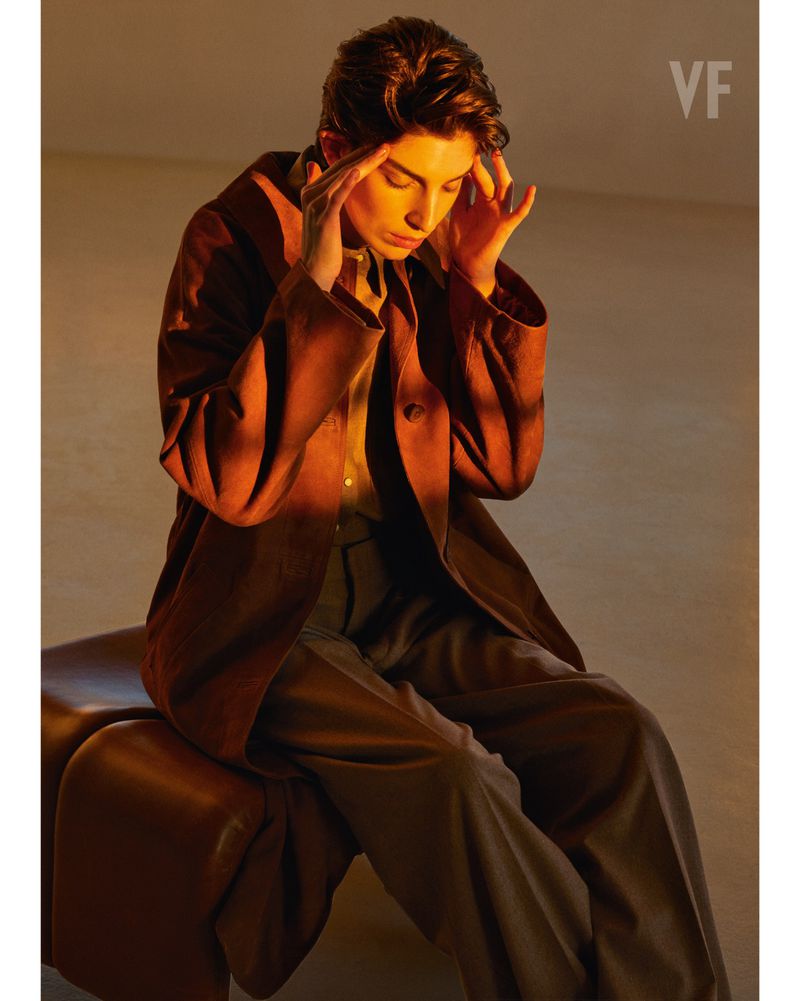 Adult woman in a brown suit sits in studio with hands on her temples, bathed in warm, golden light. Minimalist aesthetic and editorial style.