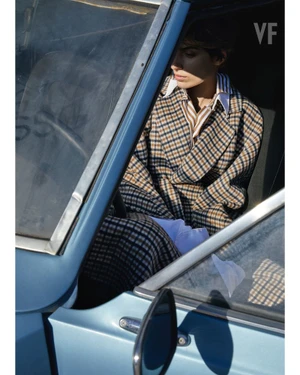 Model wearing a plaid coat seated inside a vintage blue car for Vanity Fair Italia editorial
