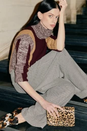 Model Lily McMenamy seated on dark steps wearing a color-blocked turtleneck sweater and houndstooth trousers