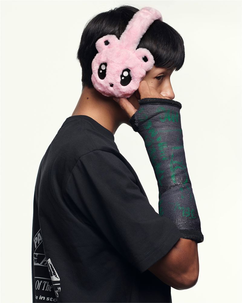 Person wearing pink fuzzy bear earmuffs and black short-sleeve shirt with arm in textured green and black cast against white backdrop.