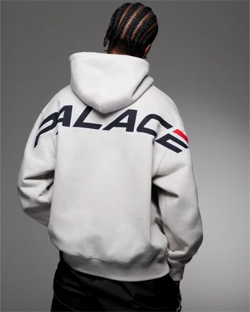 Back view of an adult male wearing a white Palace hoodie with black accents and braided hair, set against a gray background.