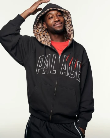 A smiling Black man wearing a black zip-up hoodie with a leopard-print lined hood poses in front of a neutral-colored background.