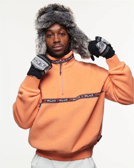 Fashionable adult male in a fleece jacket and fur hat poses indoors against a white background, showcasing stylish winter attire.
