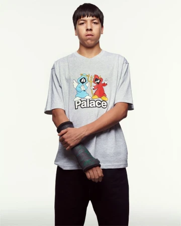 Young man wearing a grey graphic t-shirt and dark trousers standing against a plain white studio background.