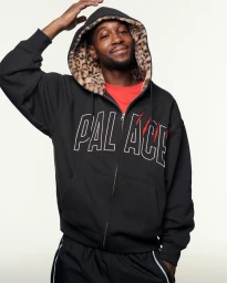 Man wearing a black zip-up hoodie with a leopard print hood liner posing against a plain background for Palace Holiday 25.