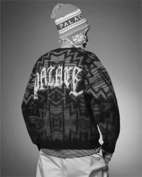Monochrome fashion photograph of a person wearing a patterned sweater with lettering and a branded beanie hat