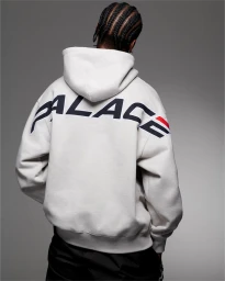 Man facing away wearing a white hoodie with large PALACE lettering across the back against a grey backdrop