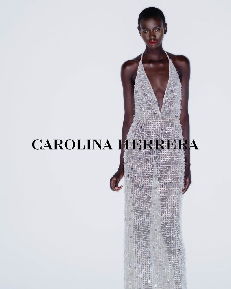 Elegant woman in a shimmering Carolina Herrera halter gown, posing against a bright white backdrop in a fashion-forward studio shot.
