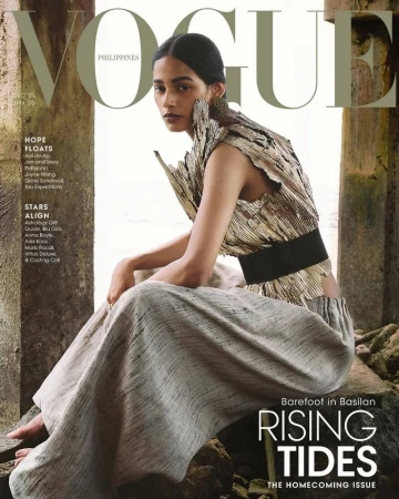 Model seated outdoors wearing a textured gold top and light grey wide-leg trousers framed by stone pillars.