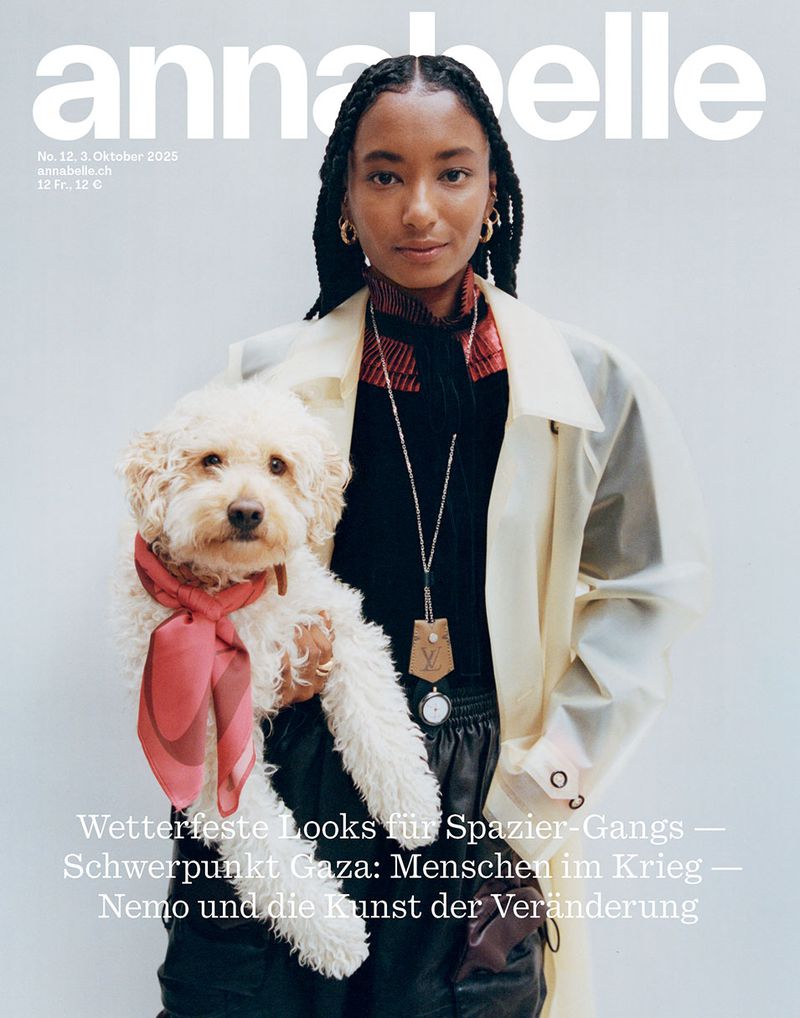 Magazine cover featuring a model holding a dog with a scarf; the model is wearing a long coat and jewelry against a light grey background.