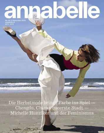 Woman in dynamic high kick holding white disc on sandy beach wearing yellow top and white skirt against ocean background