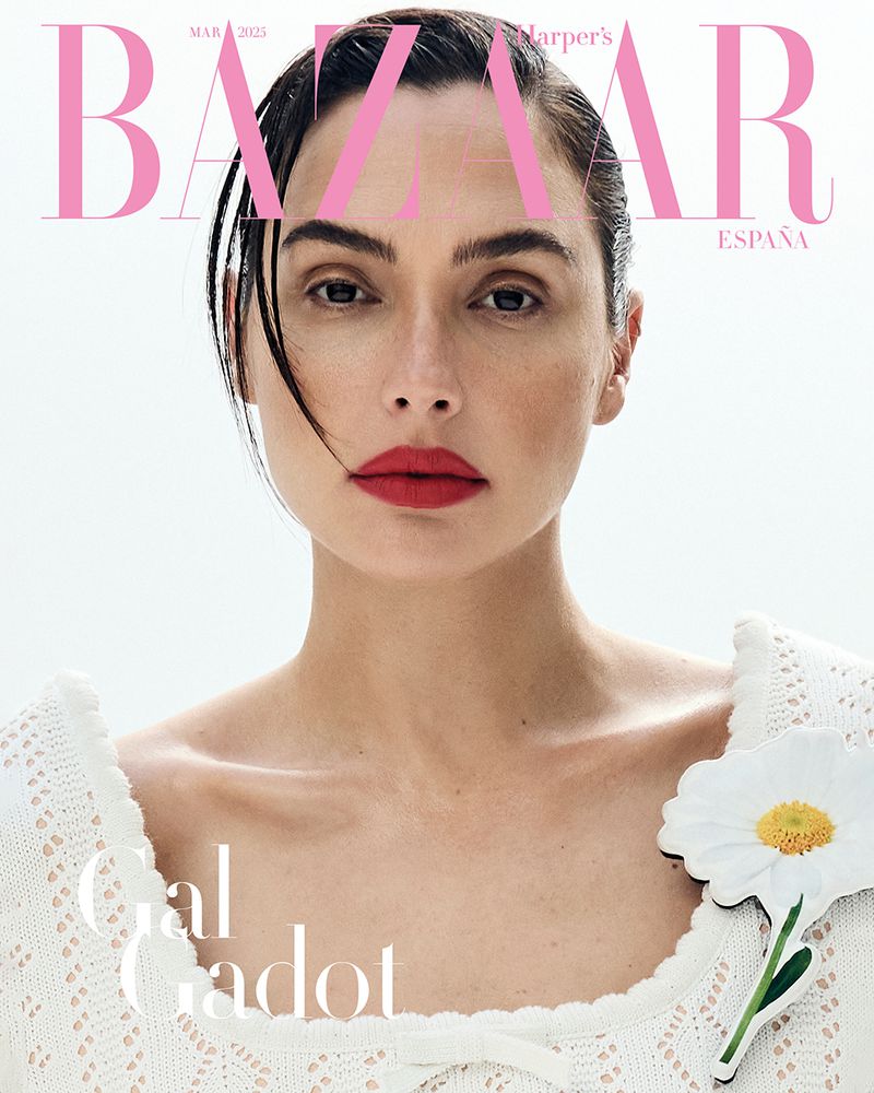 Gal Gadot's close-up on a magazine cover features her with red lipstick, wearing a white sweater with a daisy. Bright, clean style.