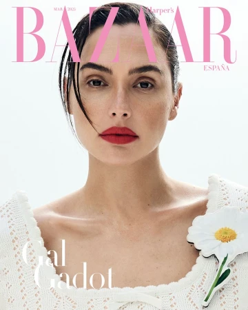 Gal Gadot's close-up on a magazine cover features her with red lipstick, wearing a white sweater with a daisy. Bright, clean style.