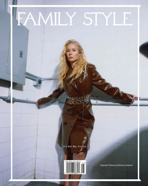 Magazine cover featuring a stylish woman in a brown patent leather trench coat with a decorative belt, posing against a white tiled wall.