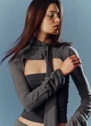 Model with long brown hair wearing a grey cutout top against a neutral studio backdrop, photographed by Julian Schulz.