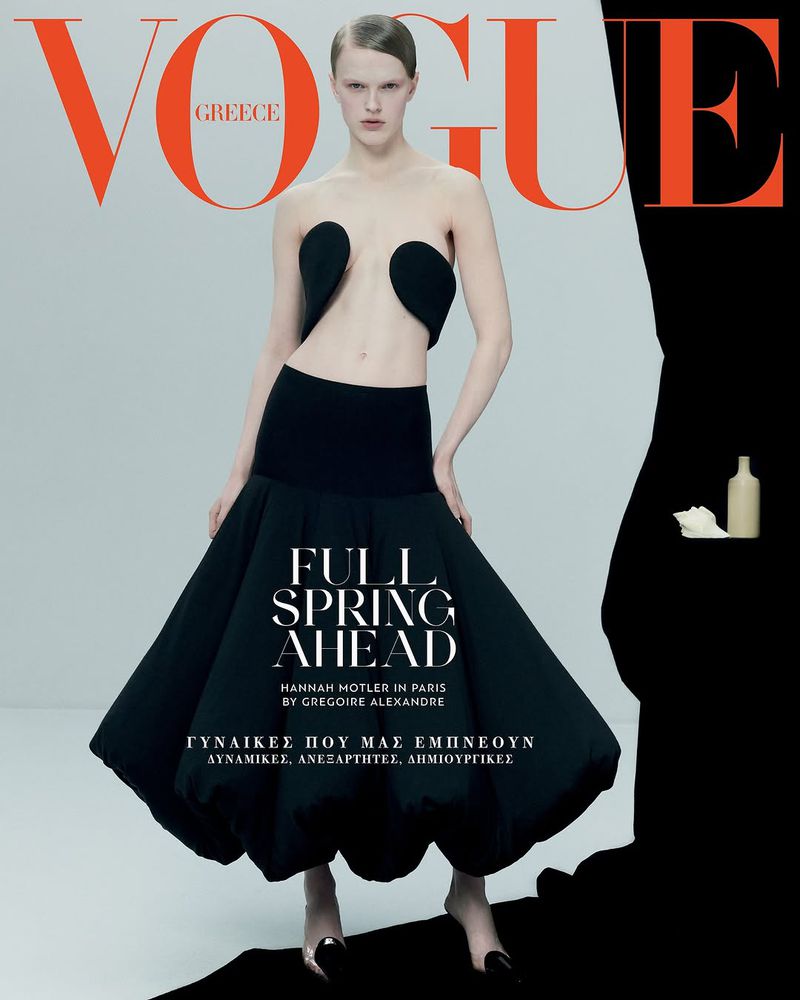 Vogue Greece cover featuring a woman in avant-garde black skirt and top, orange logo, posing in a studio setting with black accents.