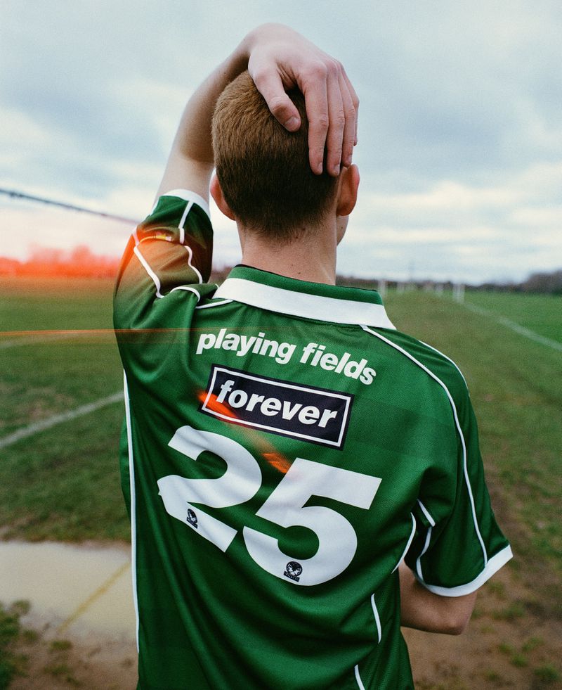Adult male in a green jersey with the number 25, standing on a sports field with grass. The sky is overcast.