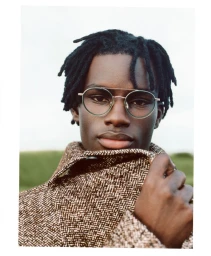 Portrait of a black man wearing round eyeglasses and pulling up a patterned brown winter coat collar