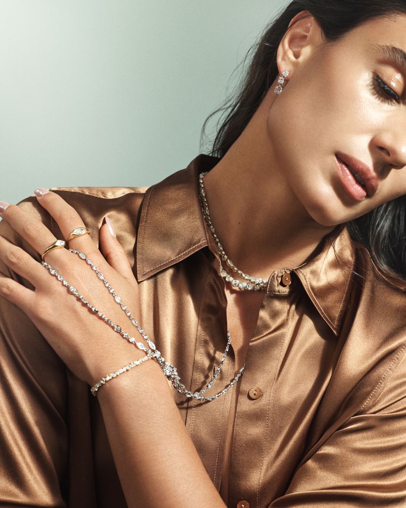 Woman with dark hair and light skin poses in a brown satin shirt, showcasing an elaborate diamond necklace and matching earrings and rings.