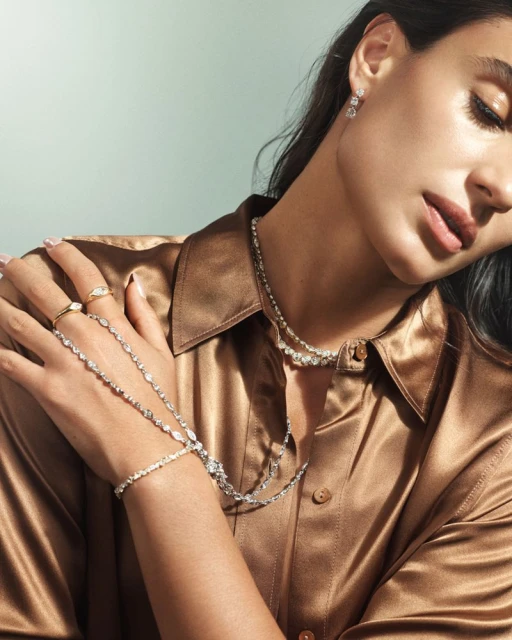 Woman with dark hair and light skin poses in a brown satin shirt, showcasing an elaborate diamond necklace and matching earrings and rings.