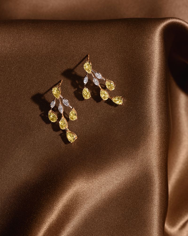 Elegant gold drop earrings featuring yellow gemstones and small white diamonds on a brown satin fabric background.