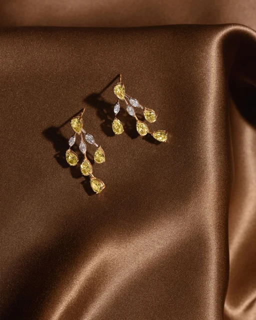 Elegant gold drop earrings featuring yellow gemstones and small white diamonds on a brown satin fabric background.