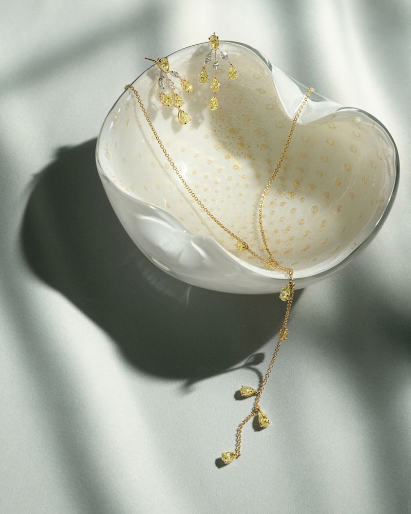 Elegant gold necklace and dangling earrings with yellow gemstone accents, displayed in a decorative white dish against a smooth backdrop.