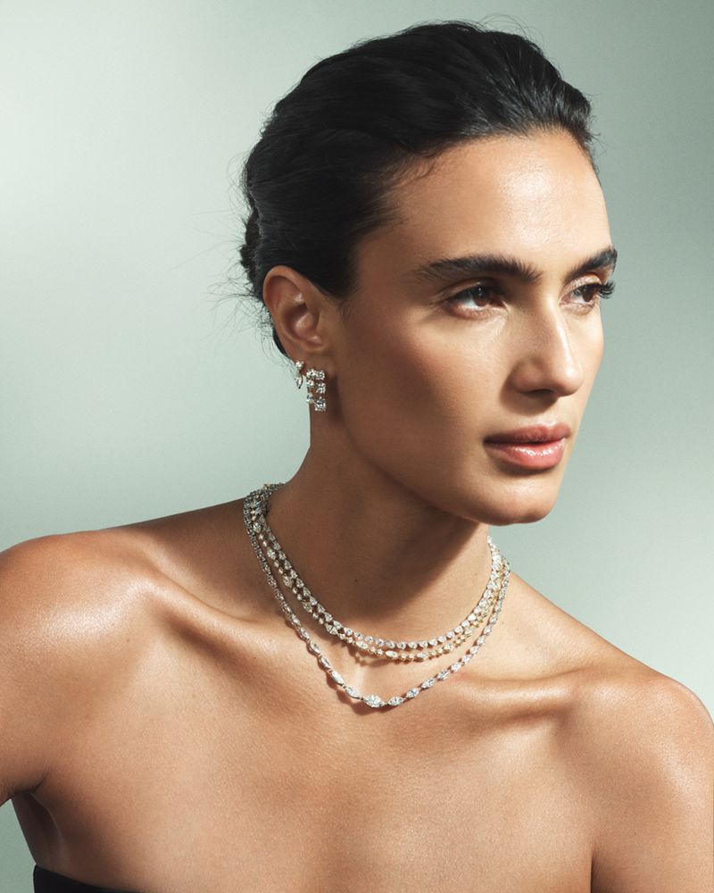 Model wearing layered diamond necklaces and matching earrings against a pale mint green studio backdrop for Isa Grutman Jewelry.