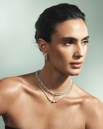 Model wearing layered diamond necklaces and matching earrings against a pale mint green studio backdrop for Isa Grutman Jewelry.