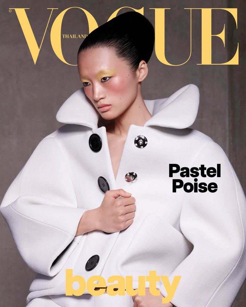 Vogue Thailand cover features a striking Asian woman wearing a large, pale overcoat and yellow eyeshadow against a gray background.