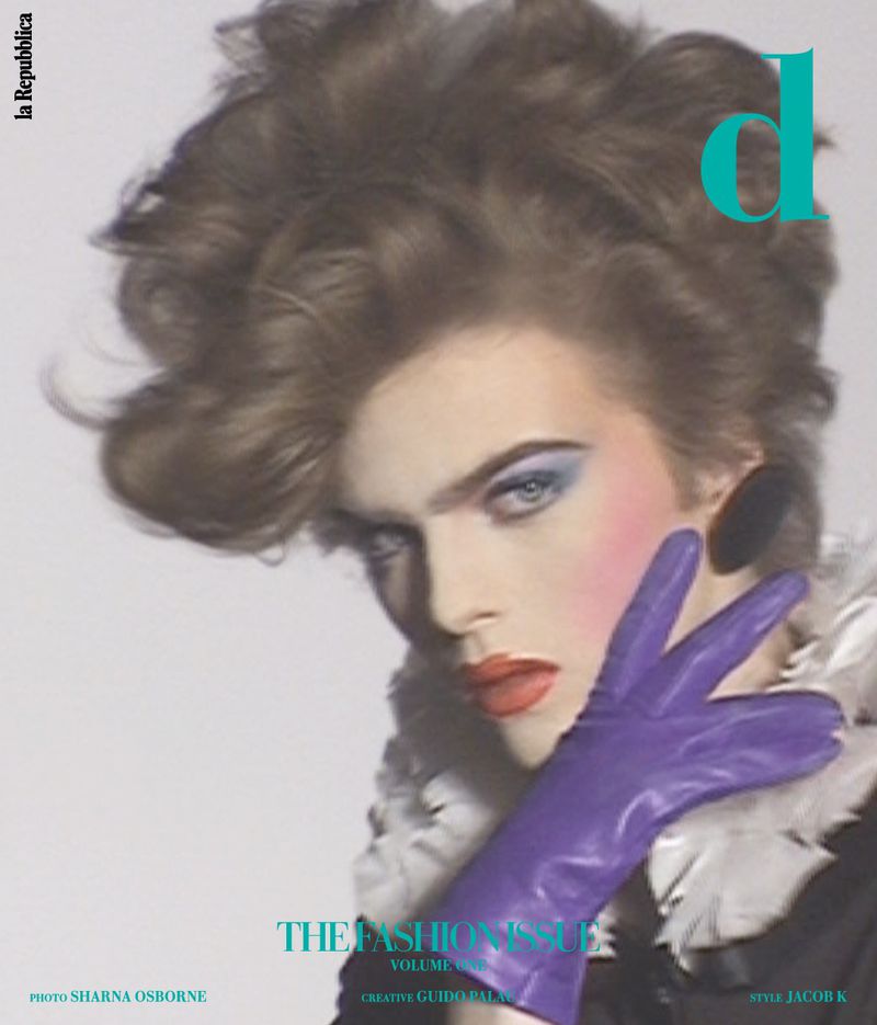 Fashion magazine cover featuring a person with dramatic makeup, voluminous brown hair, purple glove, and bold cyan and white font.