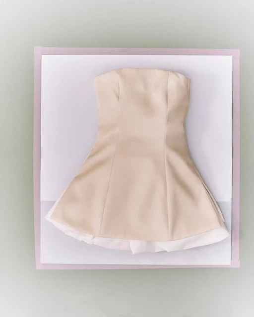 Strapless light beige dress with a white lining, displayed on a white surface with a lavender border, casting a soft shadow.