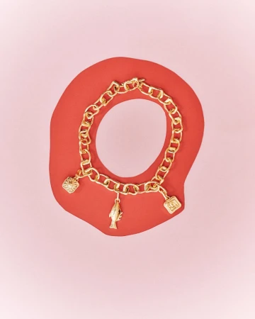 Gold charm bracelet featuring charms shaped like a heart, fish, and logo against a salmon background, jewelry concept, studio shot.