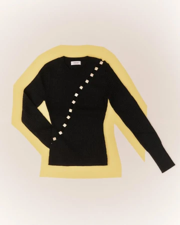 Flat lay product shot of a black knitted long-sleeve sweater featuring a diagonal row of square buttons against a yellow and off-white background