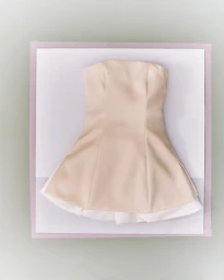Beige strapless mini dress displayed flat on white and pastel pink layered paper backdrops from an overhead angle.