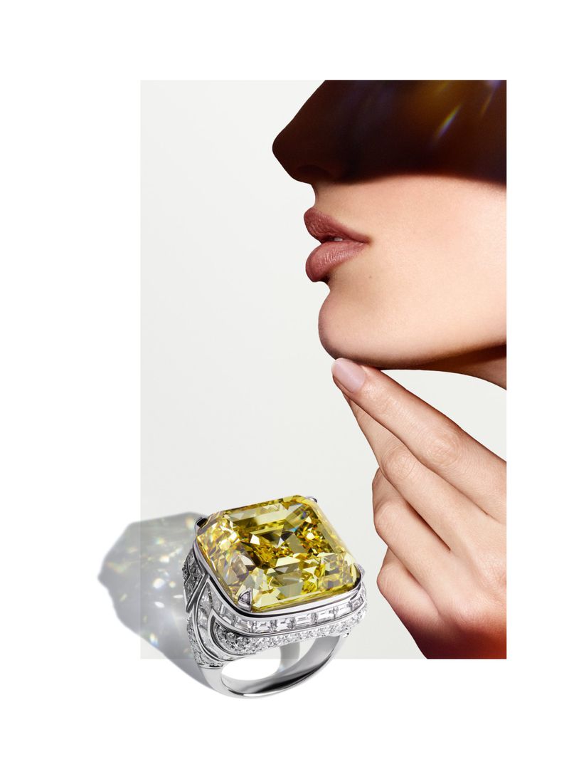 Cropped studio shot of a woman's face and hand with a large yellow diamond ring, isolated on a white background.