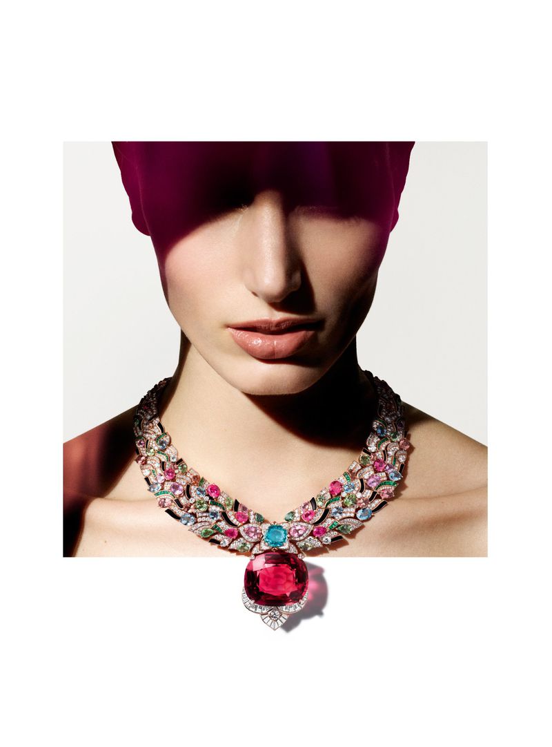 Woman wearing an elaborate gemstone statement necklace in studio lighting with a magenta light leak, showcasing jewelry fashion and beauty.