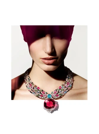 Woman wearing an elaborate gemstone statement necklace in studio lighting with a magenta light leak, showcasing jewelry fashion and beauty.