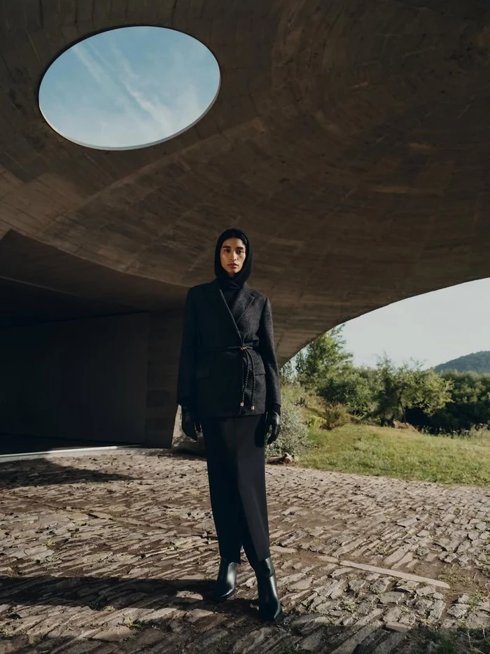 Model wearing dark blazer and skirt standing under a curved concrete structure with a circular skylight for Agnona F/W 25
