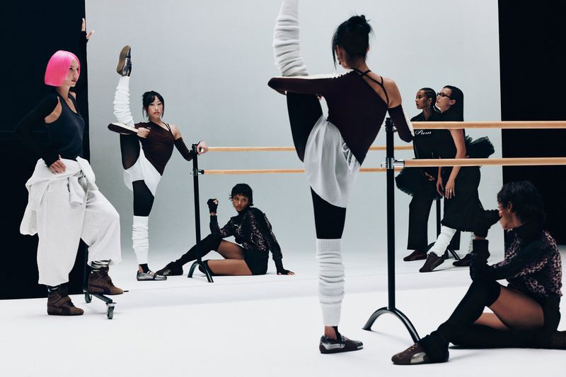 Group of young women in athletic wear strike poses and stretch in bright studio with ballet barre, creating a fitness fashion editorial.