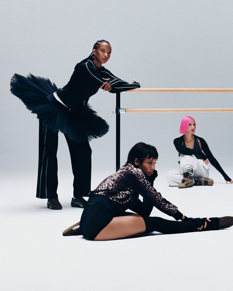 Three women model athletic and ballet-inspired fashion in a studio setting. One woman is wearing a black tutu with athletic pants and top.