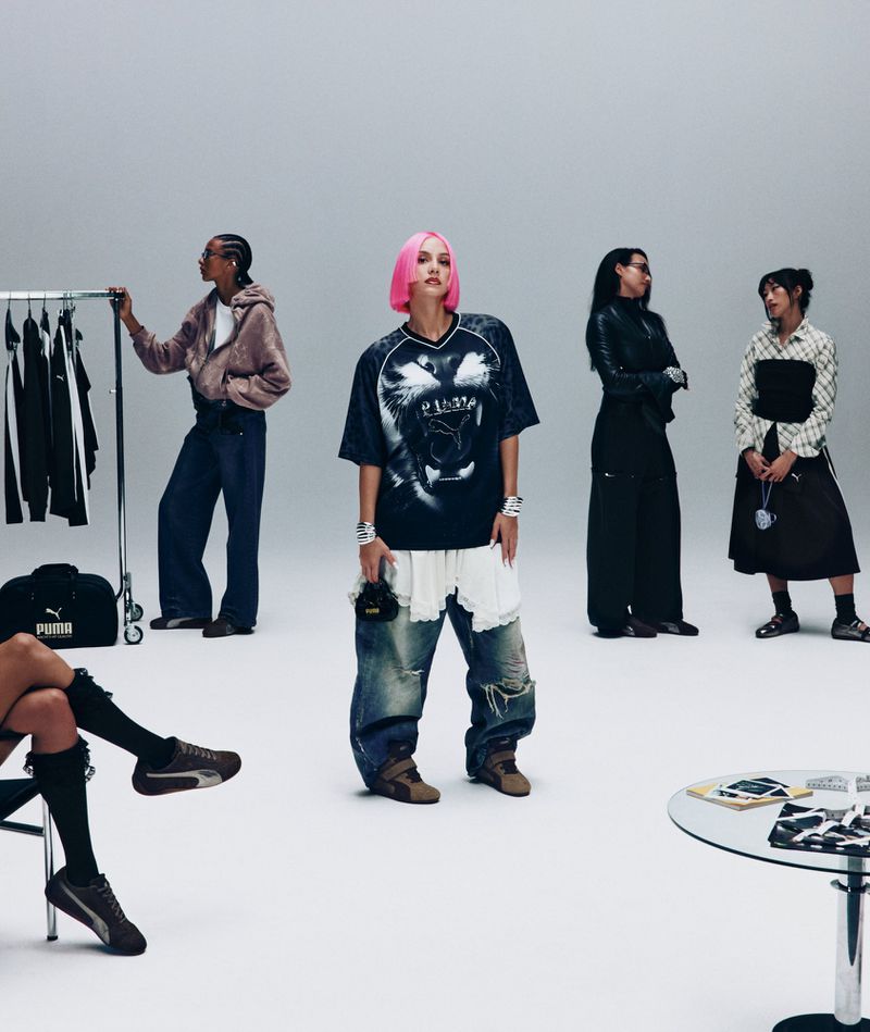 Group of five diverse people in an indoor studio setting wearing Puma clothing, standing against a light gray background with props.
