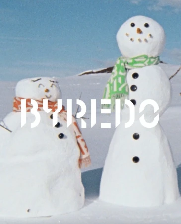 Two snowmen wearing scarves stand in a snowy landscape under a blue sky, with the BYREDO logo superimposed on the lower left.