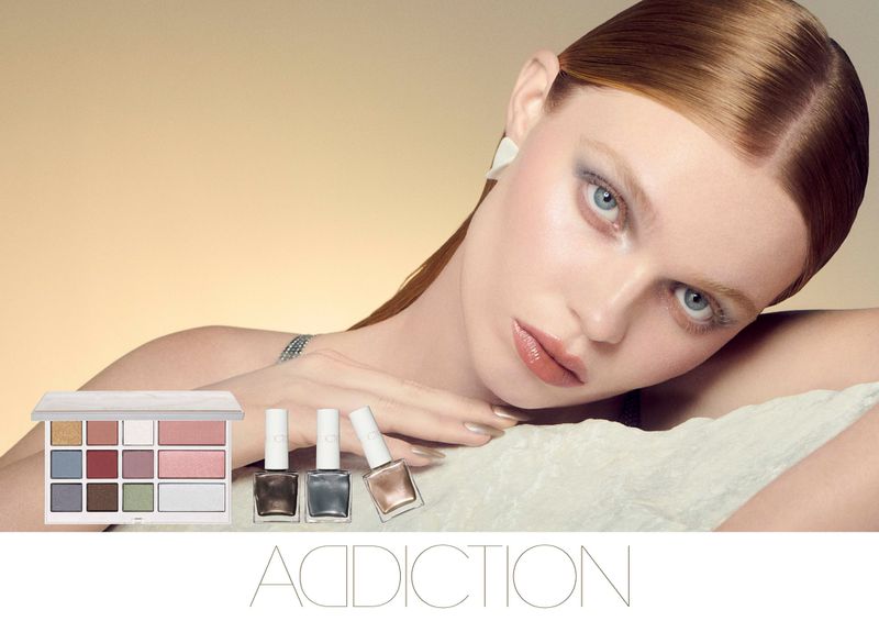 Beauty shot: A model with fair skin and red hair poses with neutral eye shadow, lip gloss, nail polish, and a makeup palette.
