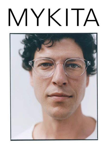 Close-up shot of a male model wearing clear-rimmed glasses against a light background, with the brand MYKITA displayed above.