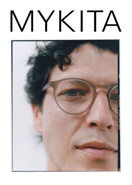 Close-up of a man wearing glasses, featuring the eyewear brand MYKITA; studio lighting enhances the clear details and clean background.